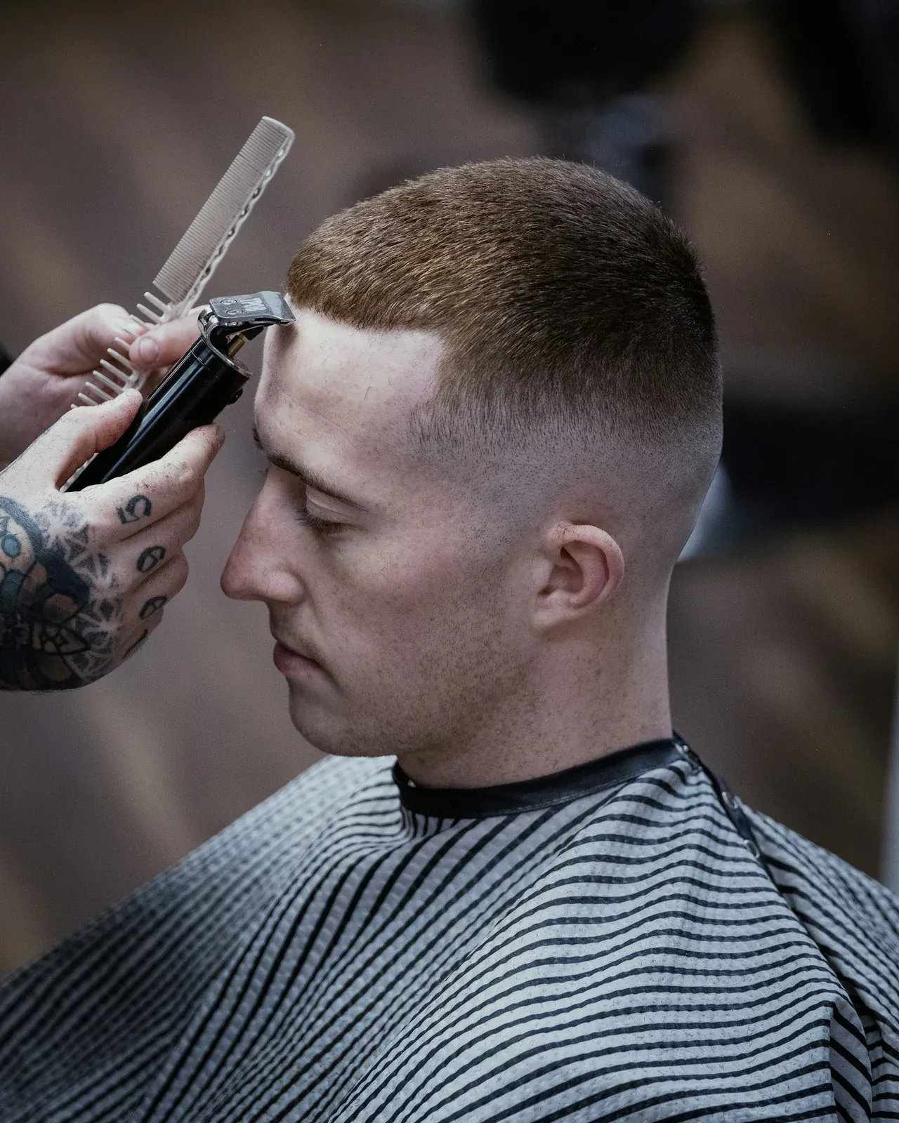 Barbeiro acertando com a máquina a linha da testa de um cliente de buzz cut com a lateral em degradê