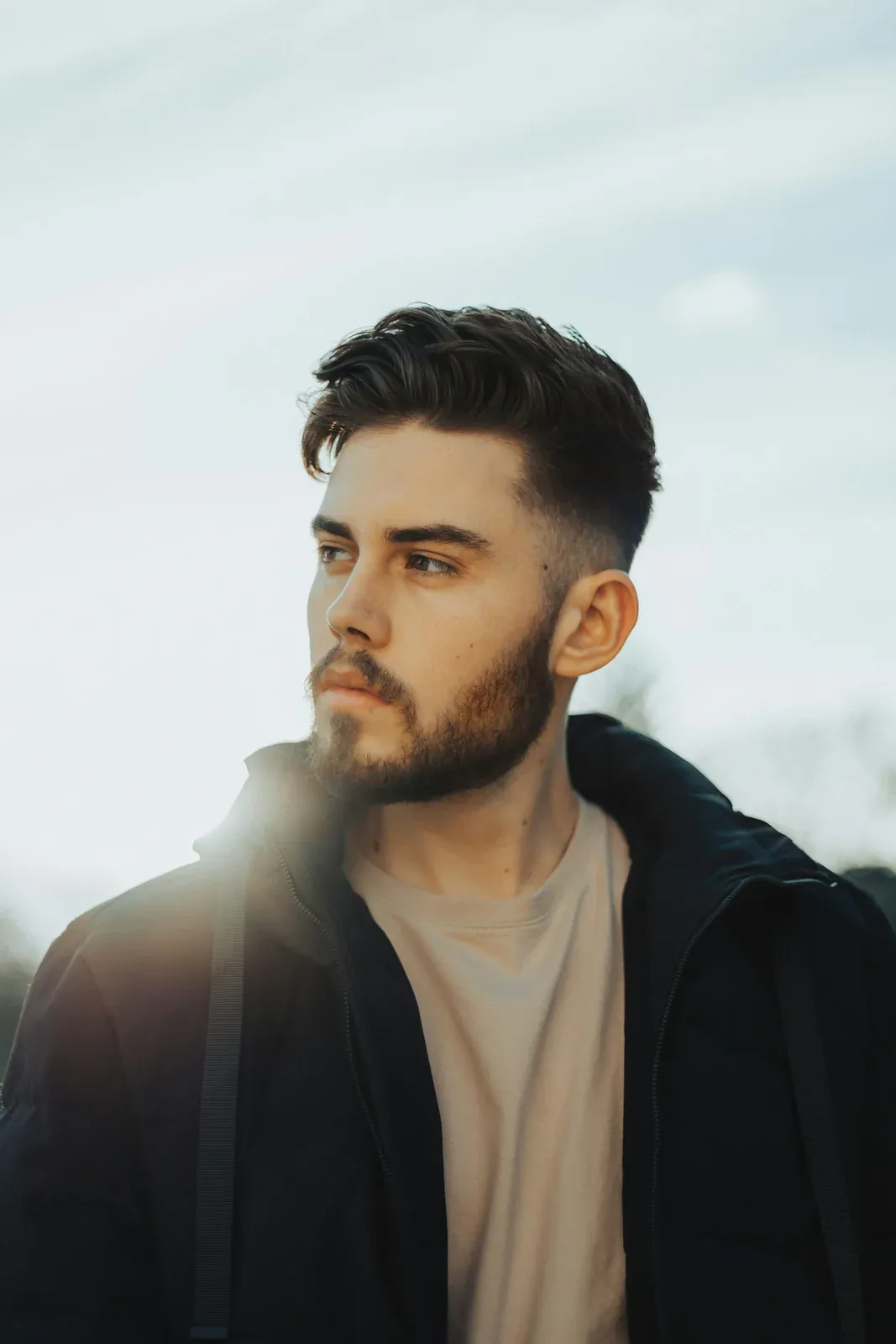 Homem de barba olhando para o lado, com a lateral em degradê baixo e o topo mais comprido penteado para trás