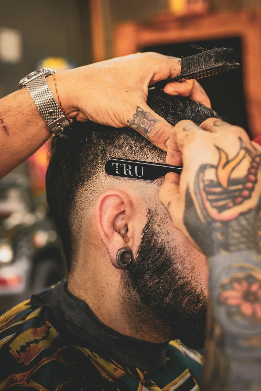 Barbeiro passando a navalha acima da orelha de um cliente de barba cheia para levar o degradê até a pele