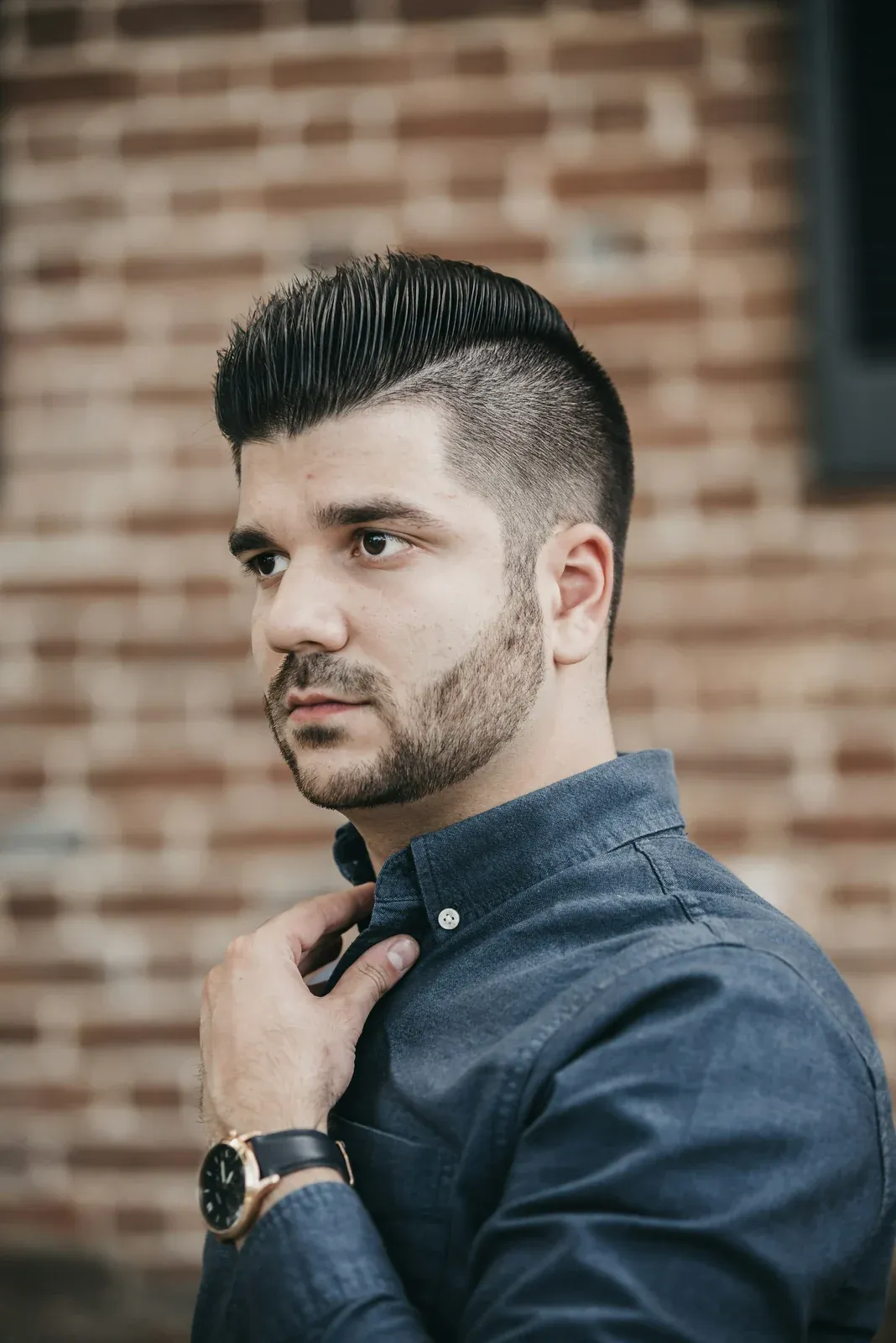 Homem de barba e camisa social com o topo penteado para cima e para trás, risca lateral e laterais curtas
