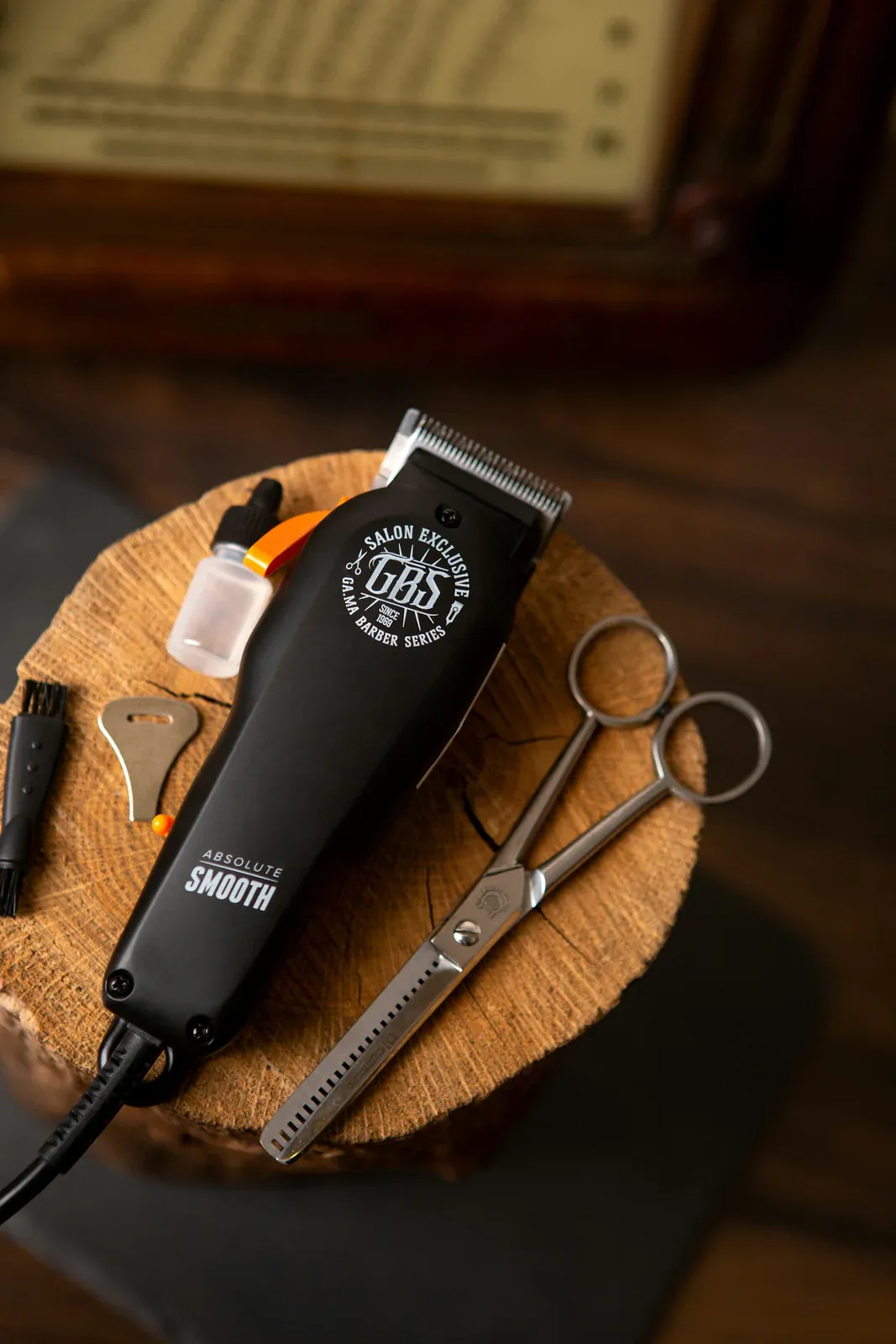 Máquina de cortar cabelo preta, tesoura de desbaste, escovinha e frasco de óleo sobre um toco de madeira
